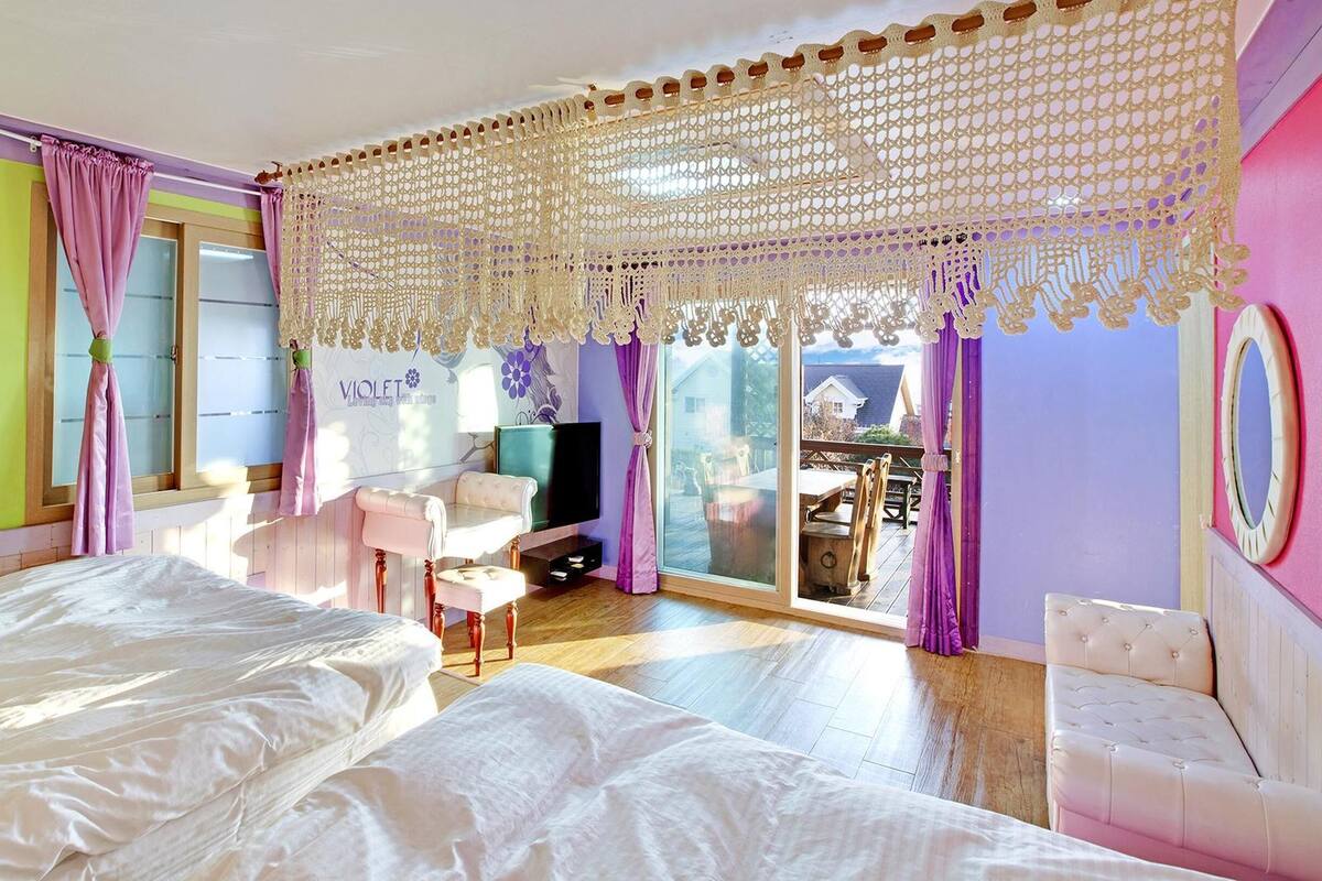 A bedroom with a large bed, a TV, and a balcony with a table and chairs.