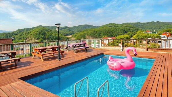 A wooden deck with a swimming pool, picnic tables, and a pink flamingo float.