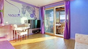 Ein Wohnzimmer mit Fernseher, einer Couch, einem Esstisch und einer Glastür zum Außenbereich.