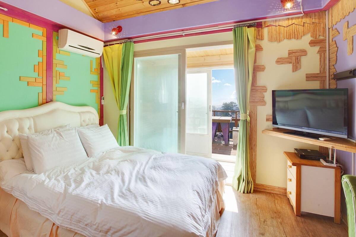 A bedroom with a bed, a television on a stand, and a window with curtains.