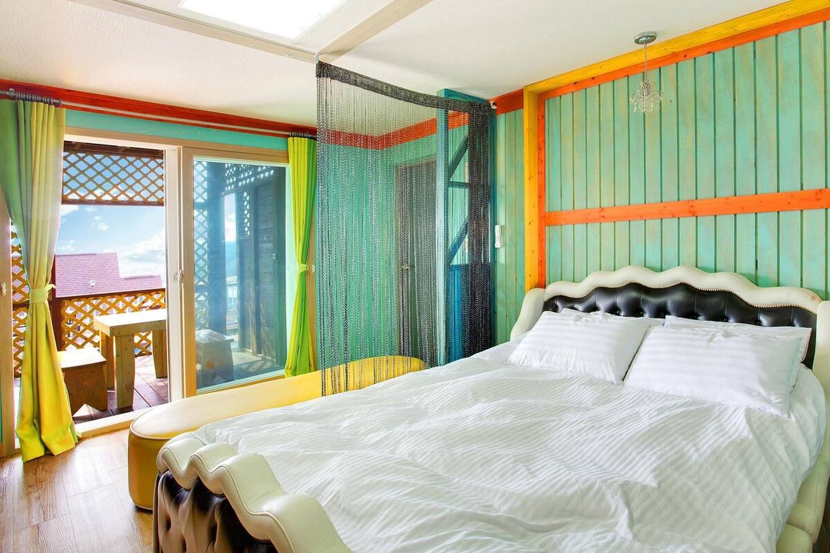 A room with a bed, a window with curtains, and a view of the outside.
