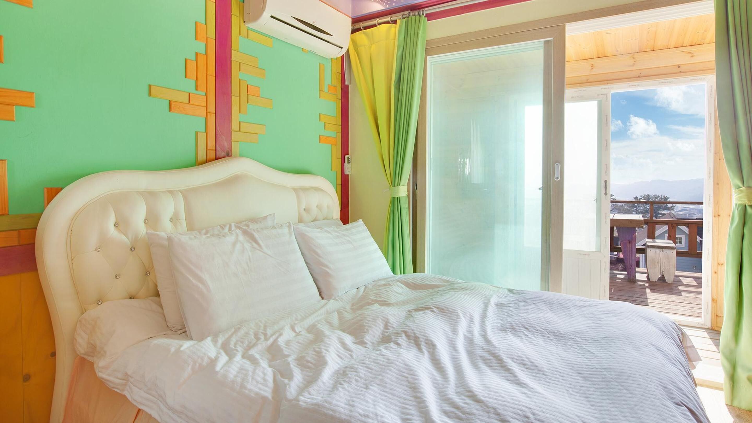 Una camera da letto con un letto bianco, una parete verde e vista sull'esterno.