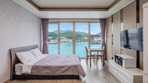 Une chambre d’hôtel avec un lit, une télévision, une table et une vue sur un plan d’eau et des collines.
