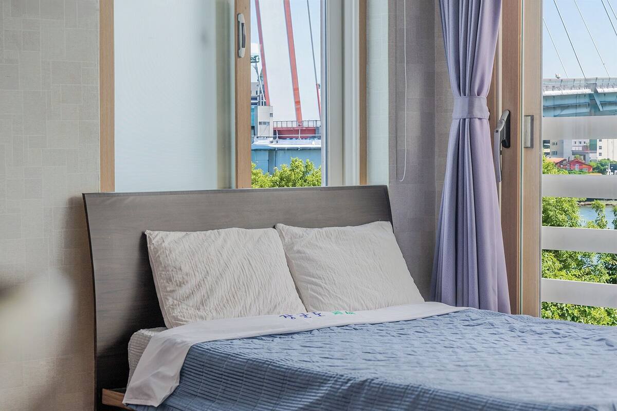 Une chambre d’hôtel avec un lit, une fenêtre donnant sur un pont et un rideau.