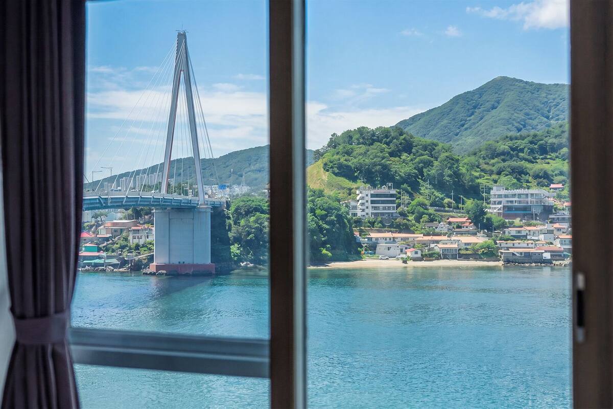 Une vue d’un pont enjambant une étendue d’eau, avec des bâtiments et des collines en arrière-plan.