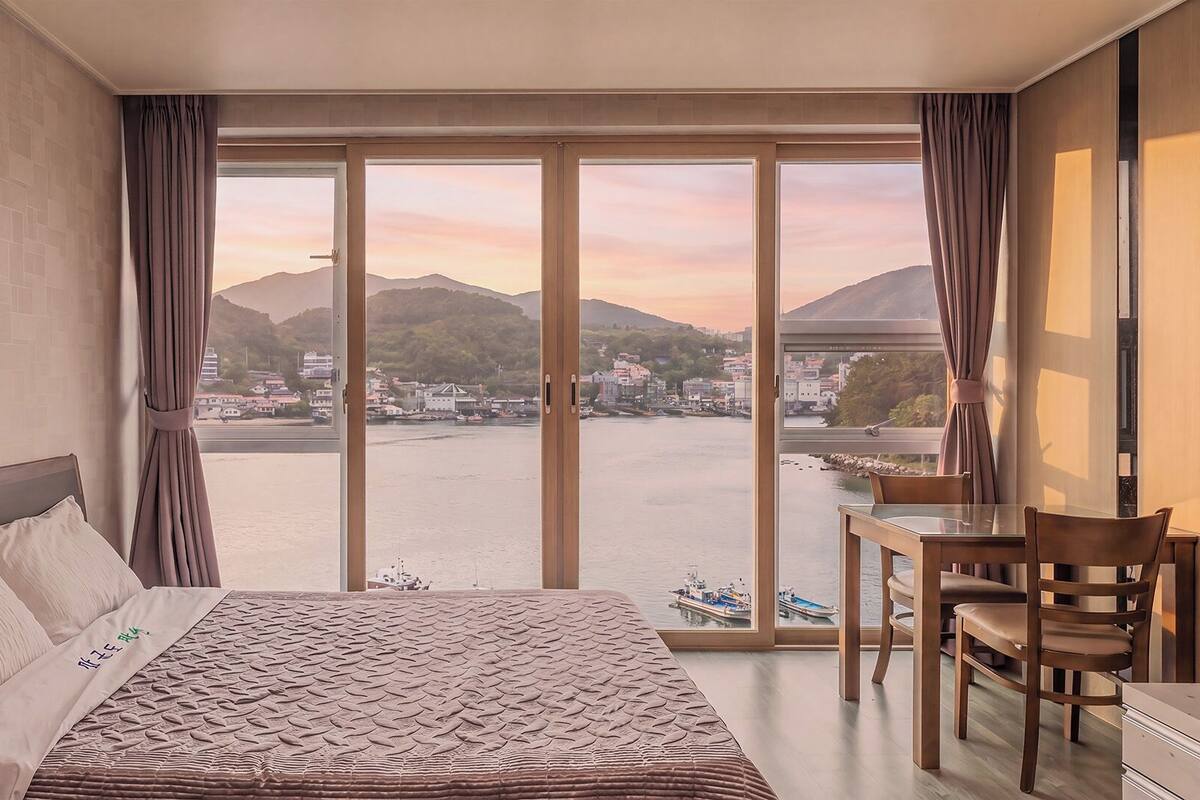 Une chambre d’hôtel avec un lit, un bureau et une vue sur un plan d’eau et des collines.