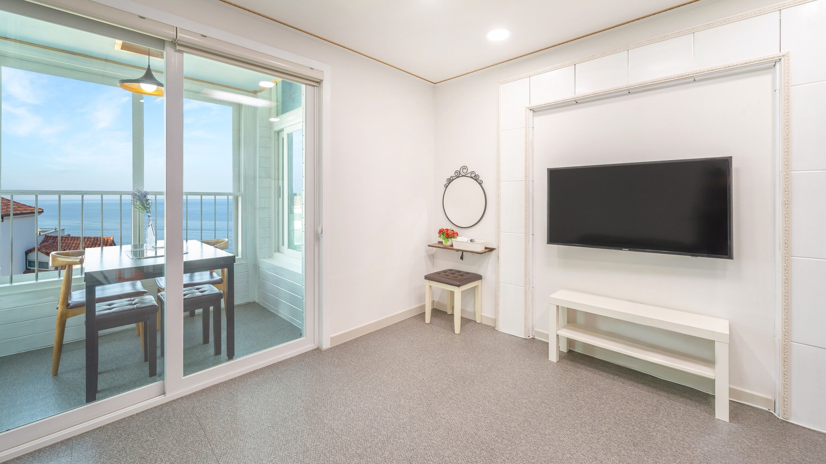 A room with a balcony, a TV, a small table with chairs, and a bench.