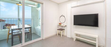 A room with a balcony, a TV, a small table with chairs, and a bench.