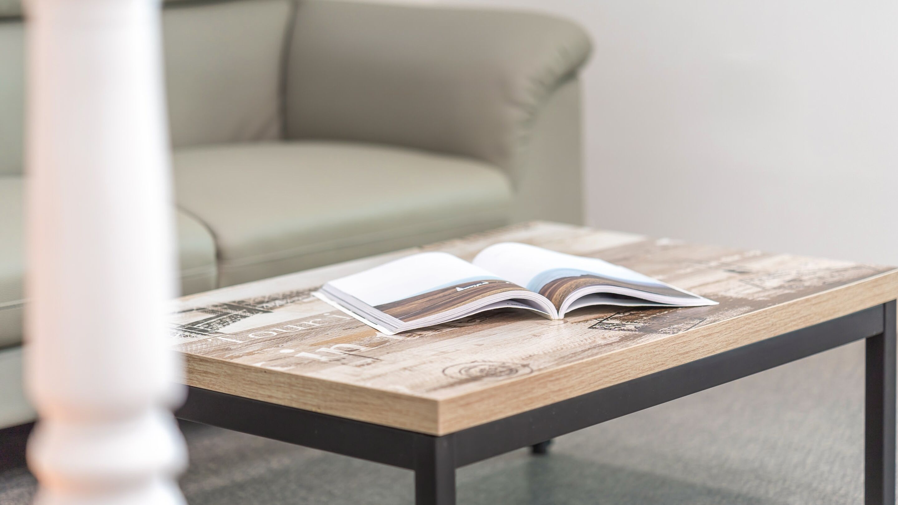 A book on a wooden table with a modern design, positioned in a room with a green sofa and a white column.