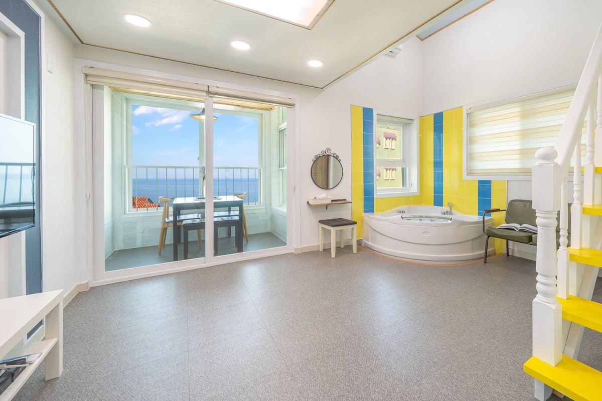 A modern interior with a balcony, a round bathtub, and a staircase with yellow accents.