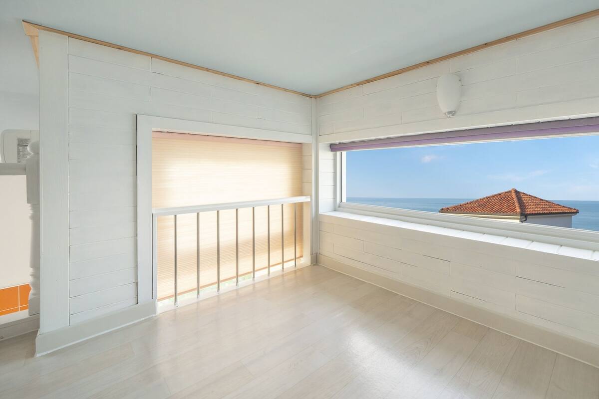 A room with a large window, wooden flooring, and a view of the sea.