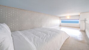 Un dormitorio con una cama grande, vista al mar por una ventana y una pared decorada.