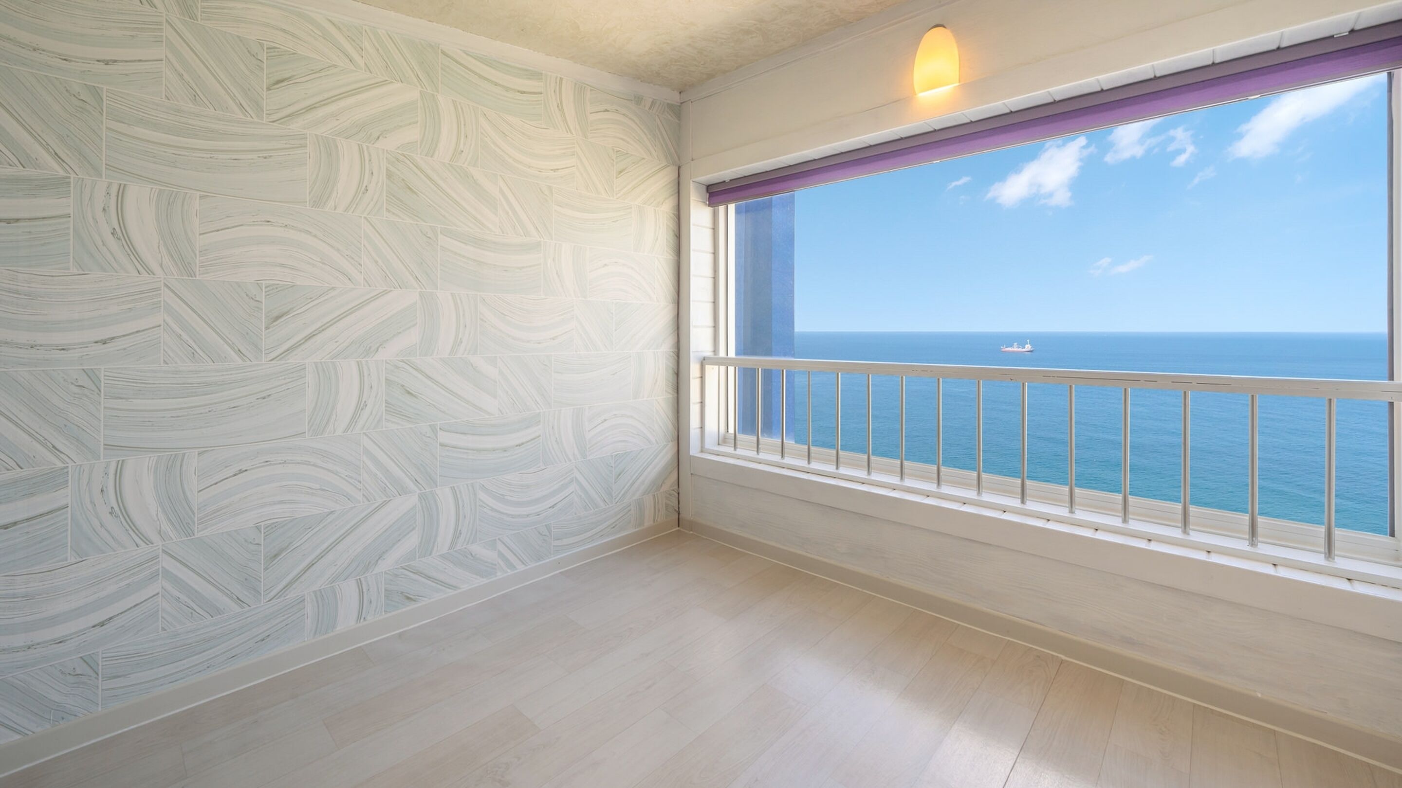 A room with a patterned wall, a window with a view of the sea, and a balcony railing.