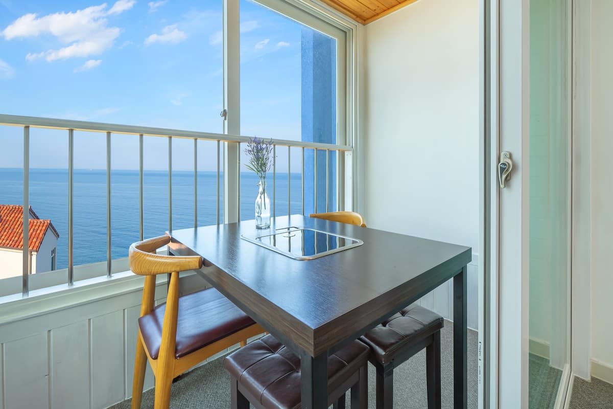 A balcony with a table and chairs, a vase with flowers, and a view of the sea.