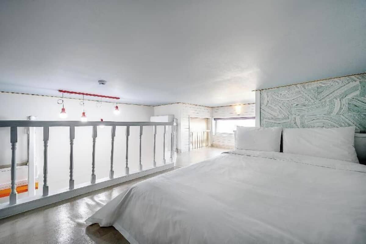 A bedroom with a large bed, a balcony with a railing, and a view of the outside.