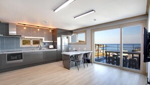 A modern kitchen with a large island, a dining area with chairs, and a view of the ocean through large sliding doors. - Donghae Haru Pension (Donghae)
