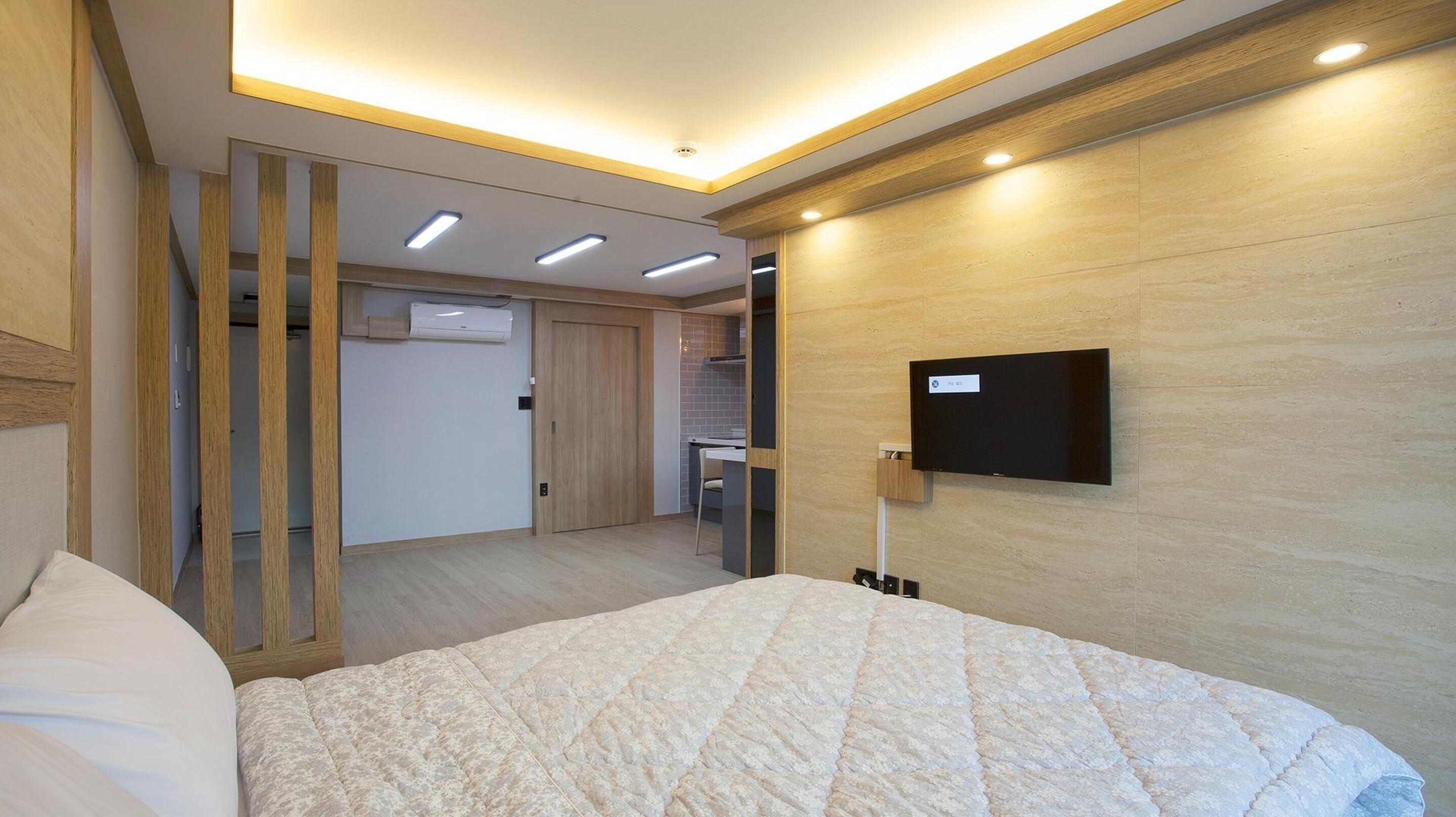 Et moderne soveværelse med en stor seng, et fjernsyn ophængt på væggen og et walk-in closet.