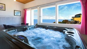 A hot tub with a view of the ocean, a dining table, chairs, and pink curtains. - Ganghwa Ana Island Pension (Incheon)