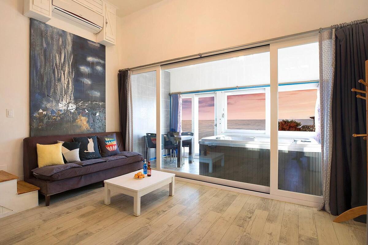 Un salon moderne avec un canapé, une table basse et une grande fenêtre donnant sur la mer.