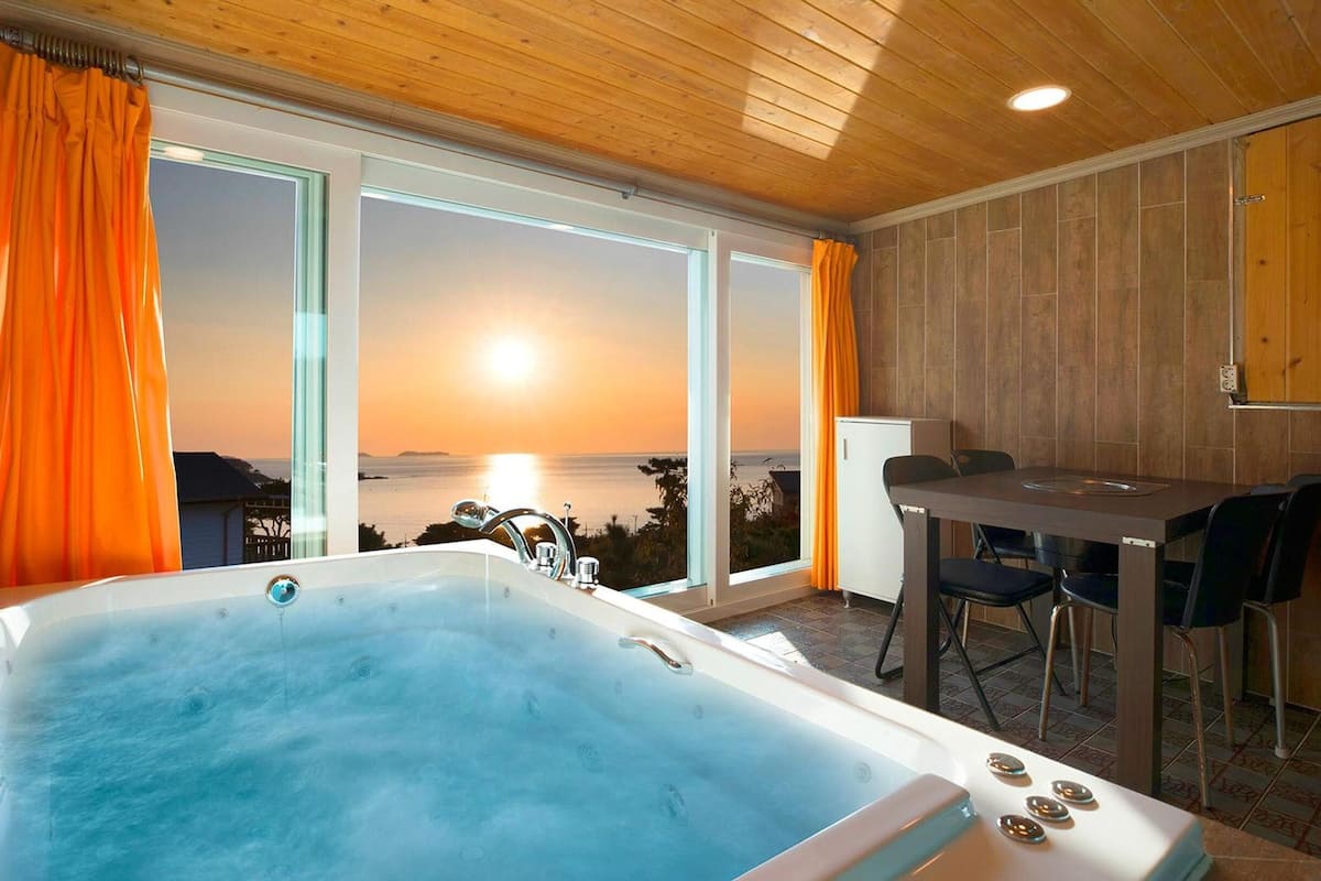 Une pièce dotée d’un jacuzzi, d’une table à manger avec des chaises et de grandes fenêtres avec des rideaux.
