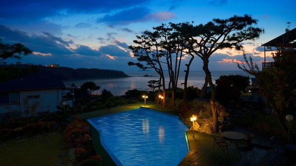 A swimming pool with a view of the sea at dusk, surrounded by trees and a small patio area. - Ganghwa Ana Island Pension (Incheon)
