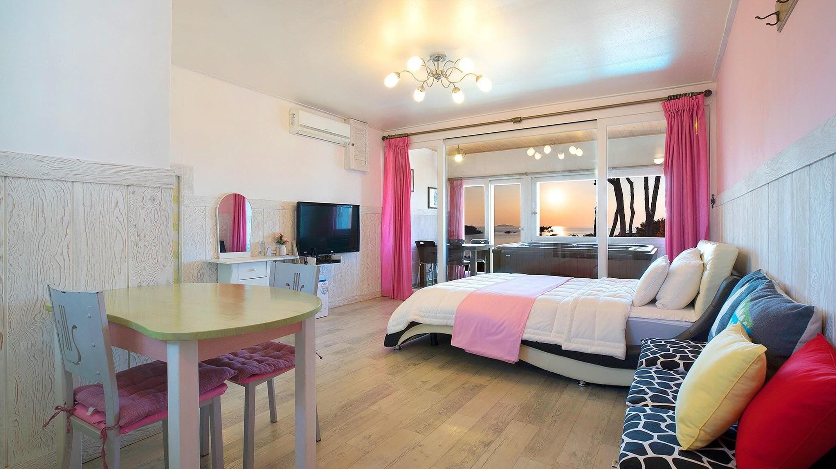 A cozy bedroom with a bed, a desk with a TV, and a view of the beach.