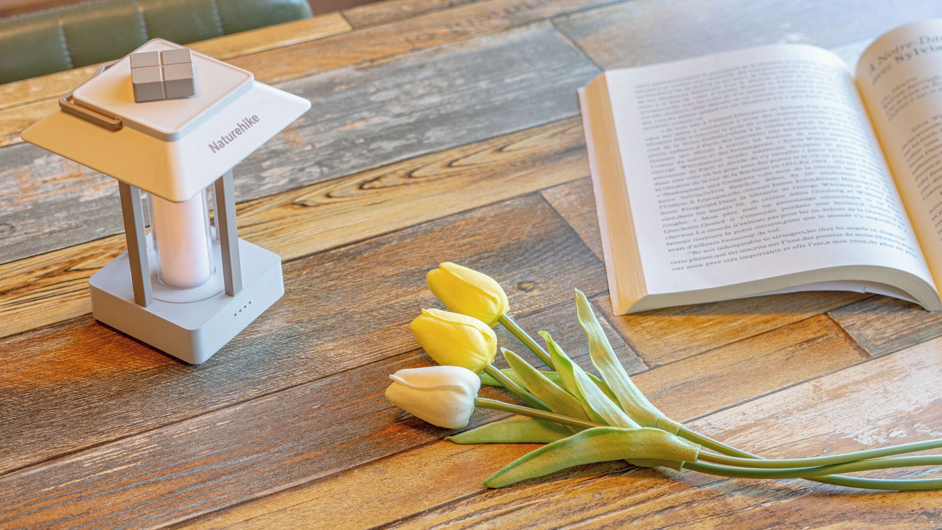 Ein Holztisch mit einer weißen Lampe, einem Buch und einem Strauß Tulpen.