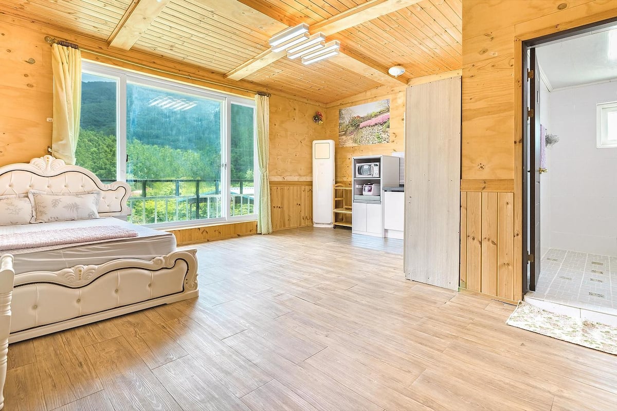 Eine Holzhütte mit einem großen Bett, einer Küchenzeile und einer Glasdoor zum Balkon.