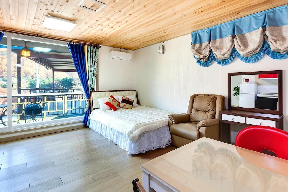 Ein Zimmer mit Bett, Stuhl, Tisch, Spiegel und Blick ins Freie.