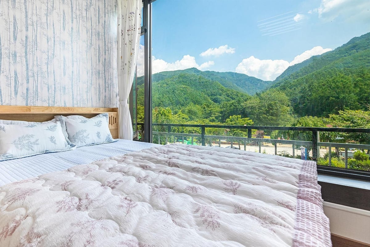 Ein Schlafzimmer mit einem Holzbett, Blumenmuster-Bettwäsche und Blick auf eine Berglandschaft vom Balkon aus.