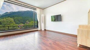 A room with a large window, a flat-screen TV, and a wooden floor.