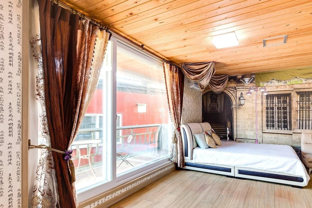 Ein Zimmer mit einem Bett, einem Schlafsofa, einem großen Fenster und Blick auf ein rotes Gebäude.