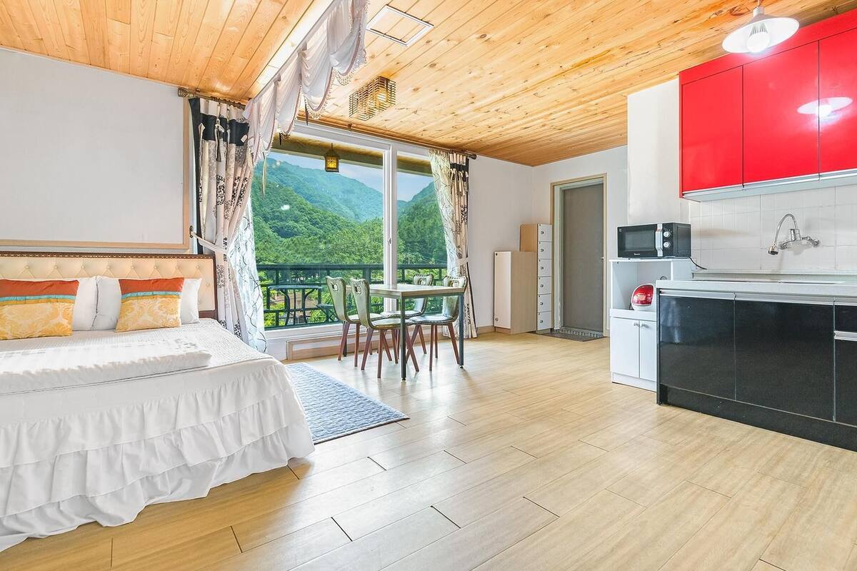 Une chambre avec un lit, un coin repas avec une table et des chaises, et une cuisine avec des placards rouges et un four à micro-ondes.