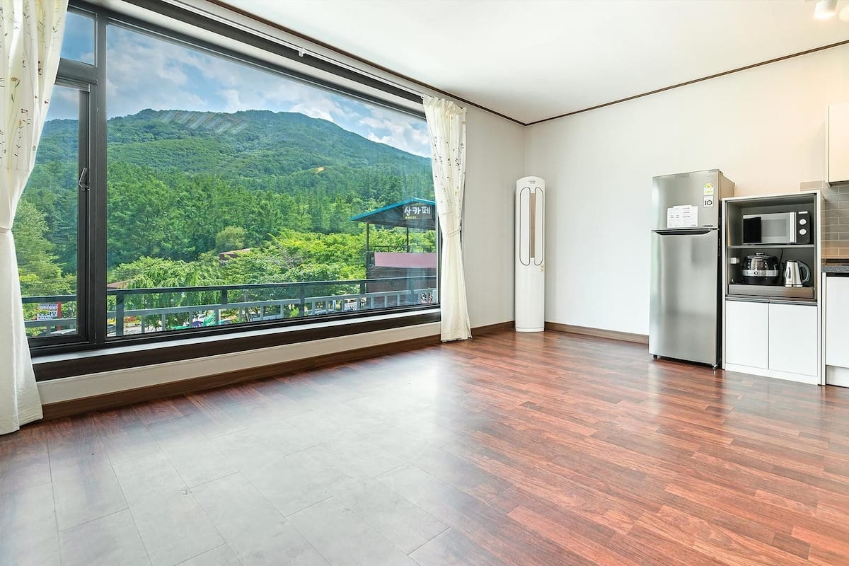 Eine moderne Küche mit großem Fenster, Holzboden und Blick auf eine grüne Berglandschaft.