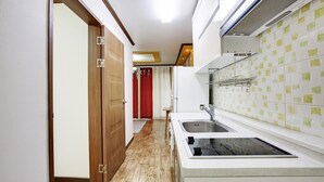 A narrow kitchen with a double sink, wooden door, and tiled backsplash. - Geoje Badasunjang Pension (Geoje)