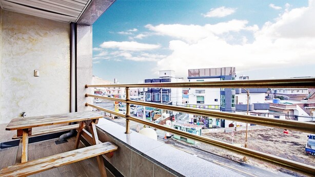 A balcony with a view of a cityscape, a wooden bench, and a railing. - Geoje Badasunjang Pension (Geoje)
