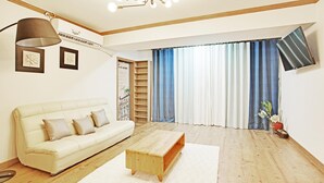 A living room with a white sofa, a wooden coffee table, and a large window with blue and white curtains. - Geoje Badasunjang Pension (Geoje)