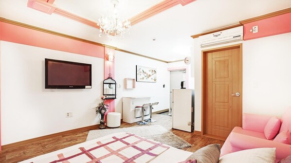 A modern bedroom with a large bed, a TV, a wooden door, and a small kitchenette. - Geoje Badasunjang Pension (Geoje)