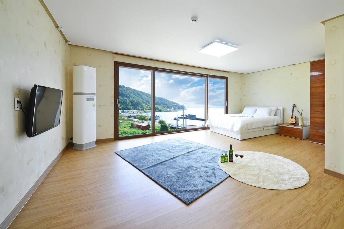 Une chambre moderne dotée d’une grande fenêtre, d’un téléviseur à écran plat, d’un lit, d’une table de chevet et offrant une vue sur la côte.