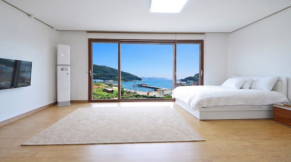 A bedroom with a large sliding glass door leading to a balcony with a view of a coastal area.