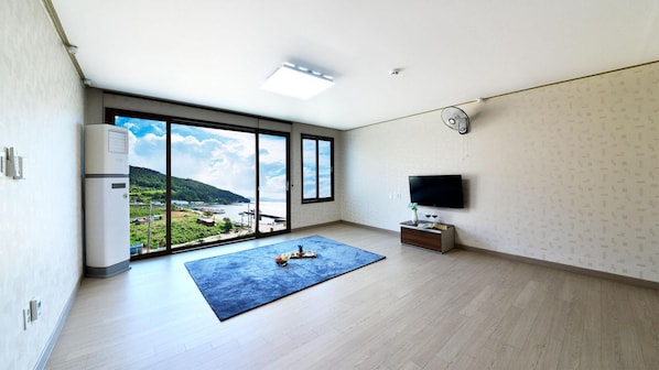 Ein geräumiges Zimmer mit einem großen Schiebeglasfenster, das auf einen Balkon führt, einem Flachbildfernseher und einer kleinen Holzkommode.