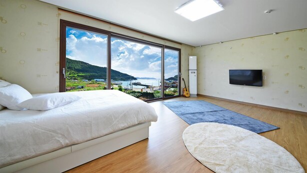Une chambre avec un lit, une télévision, une guitare et une vue sur un paysage côtier.