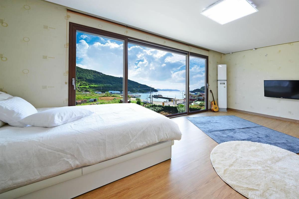 Une chambre avec un lit, une télévision, une guitare et une vue sur un paysage côtier.