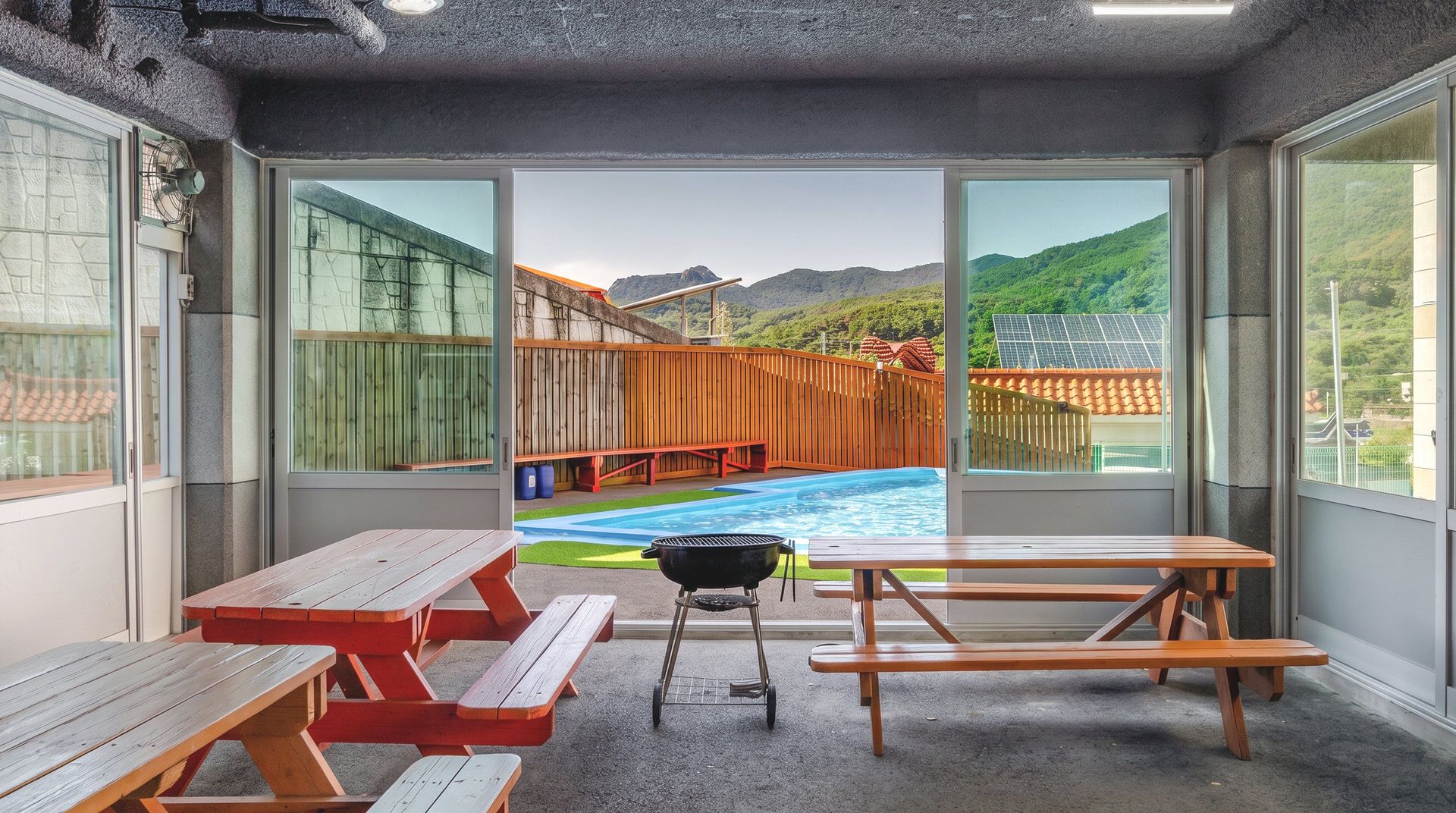 Habitación con vista a una piscina y montañas, con mesas de picnic y una parrilla.