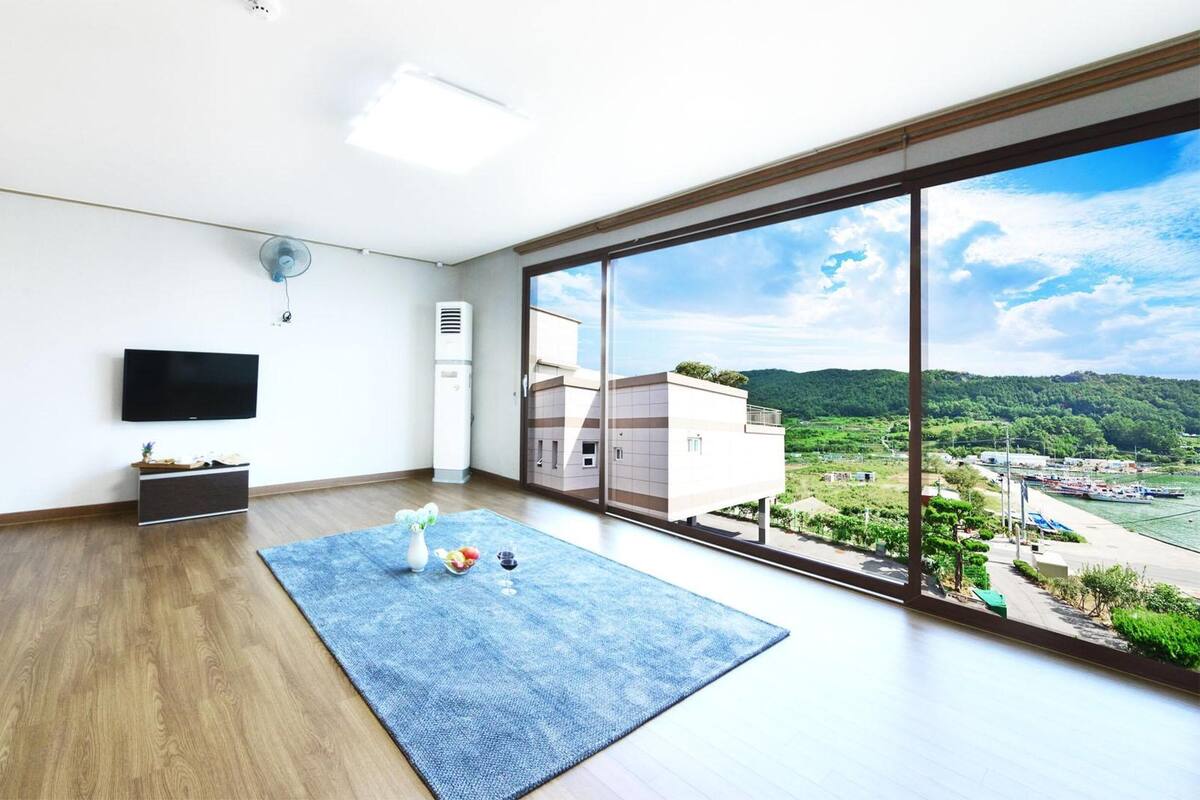 Une chambre moderne dotée d’une grande fenêtre, d’un téléviseur à écran plat, d’une petite console et d’un tapis bleu.