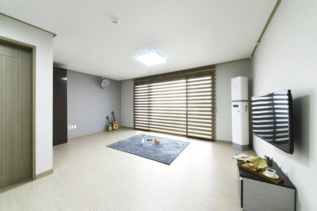 Un salon spacieux avec une grande fenêtre, un téléviseur à écran plat, une petite table avec un plateau et une guitare appuyée contre le mur.