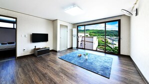 Une chambre d’hôtel moderne dotée d’une grande porte-fenêtre coulissante donnant sur l’extérieur, d’un téléviseur à écran plat fixé au mur, d’un plancher en bois et d’un tapis bleu.