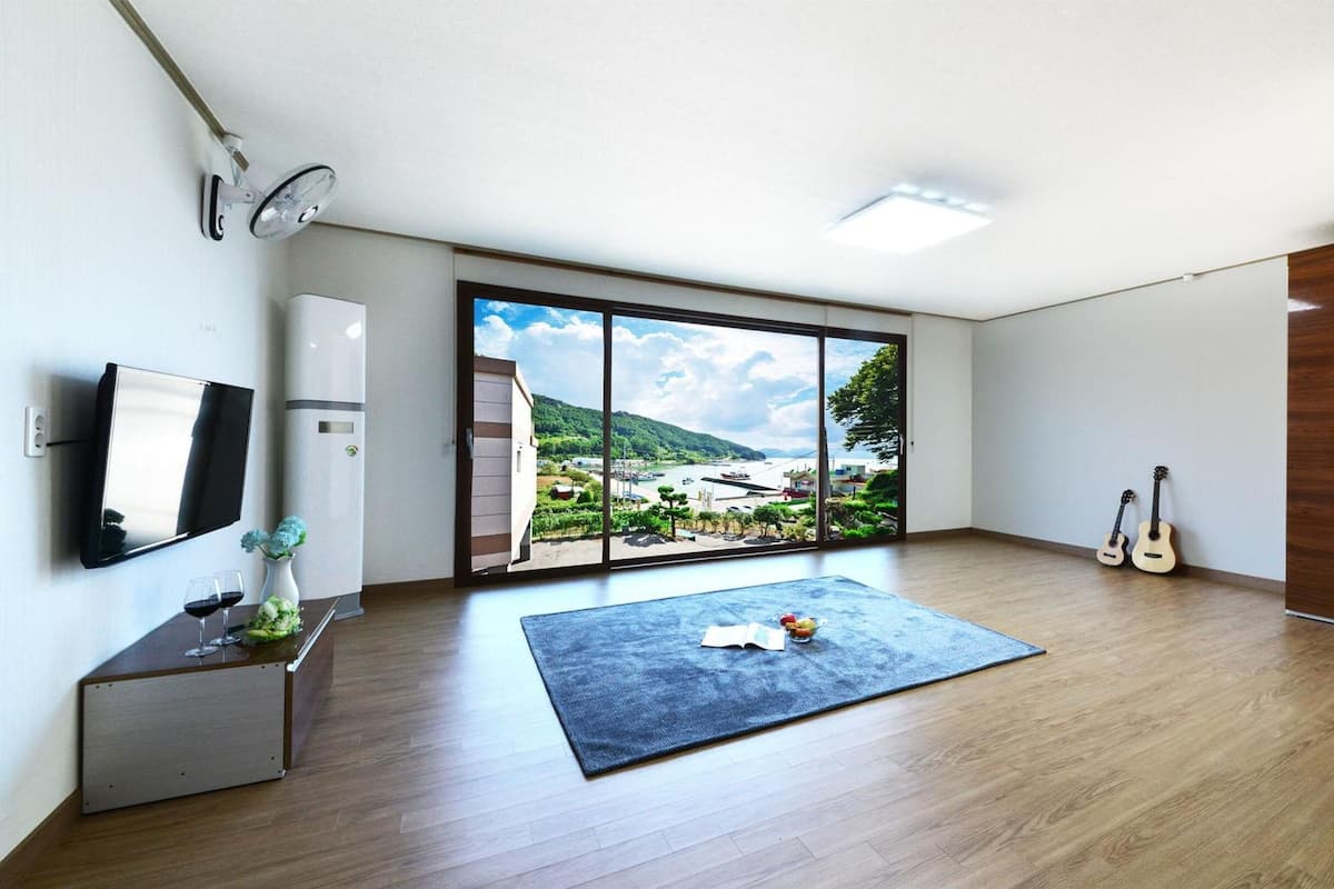 Une chambre moderne dotée d’une grande porte-fenêtre coulissante donnant sur un paysage extérieur magnifique, d’un téléviseur à écran plat, d’un petit bureau agrémenté d’un vase et de verres, et de deux guitares adossées au mur.