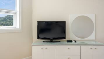 Una habitación moderna con una televisión de pantalla plana sobre un mueble de vidrio, un espejo ovalado grande y una ventana con vistas a un bosque.
