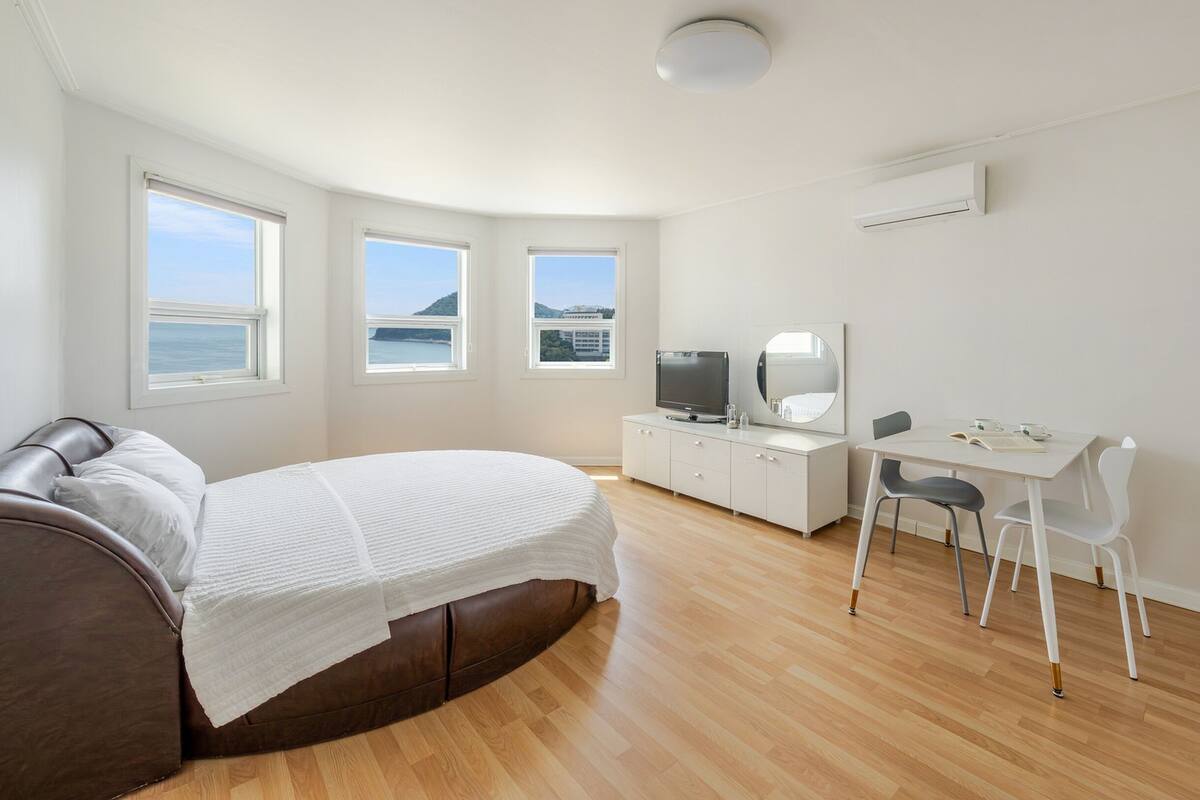 A modern bedroom with a bed, a desk, a chair, and a TV.